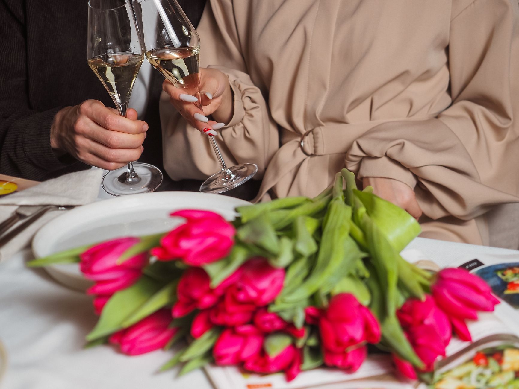A bouquet of pink tulips on a dining table beside two people holding champagne glasses