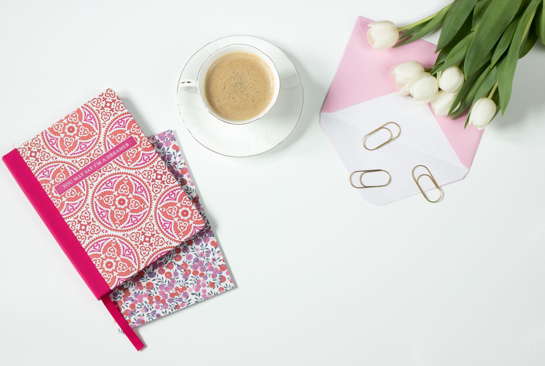 White tulips, a coffee cup, notebooks, and paper clips on a clean desk