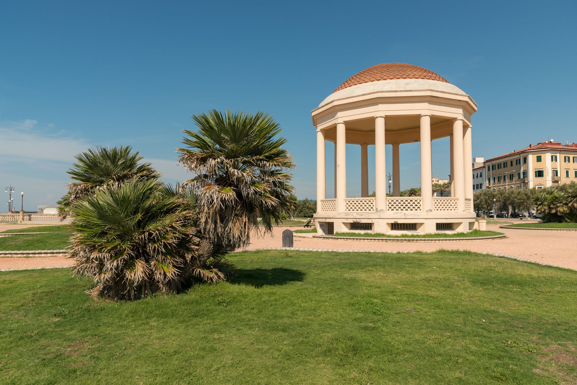 A small domed pavilion on a grassy park lawn under a clear blue sky