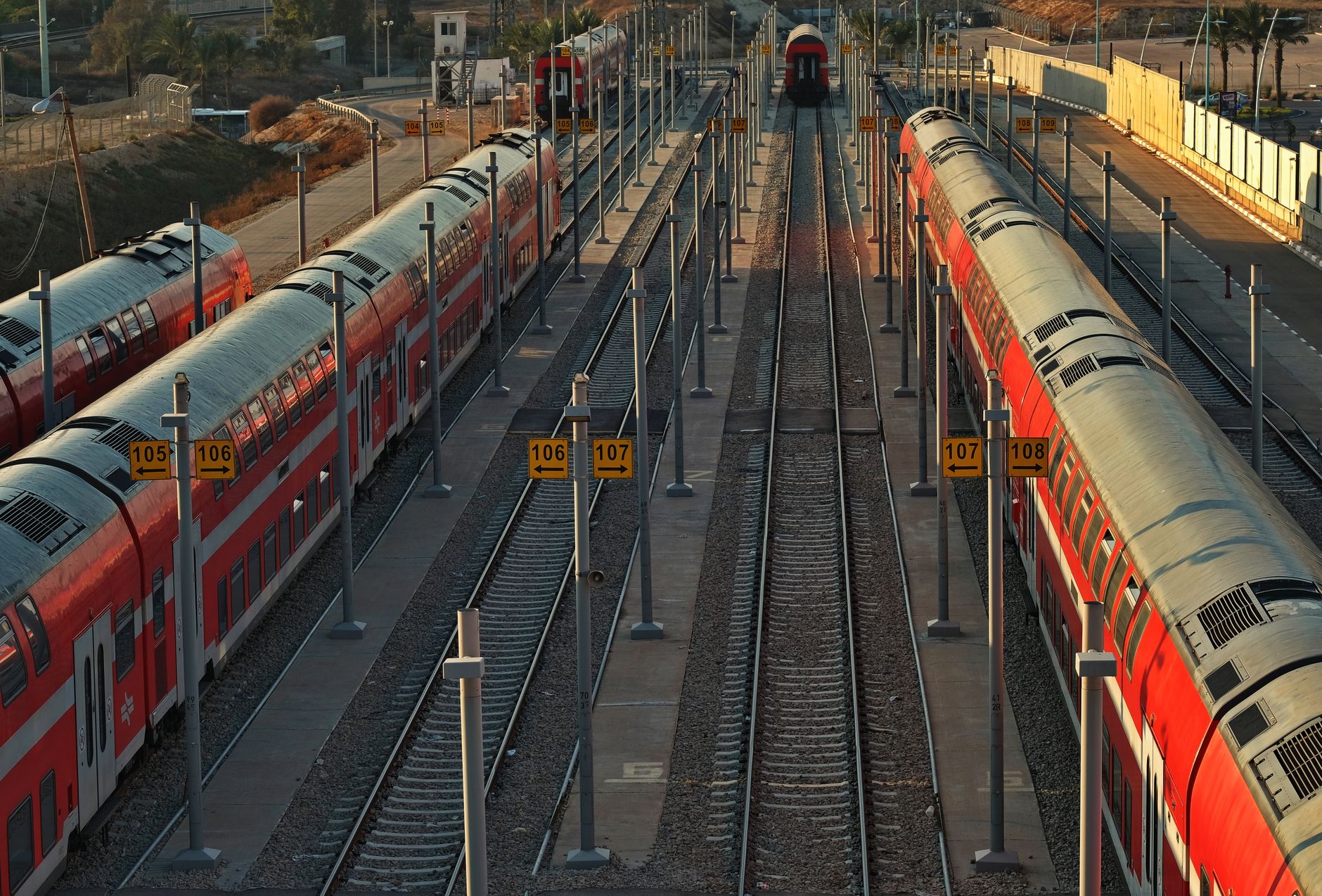 Several red commuter trains on parallel tracks at an outdoor rail station seen from above
