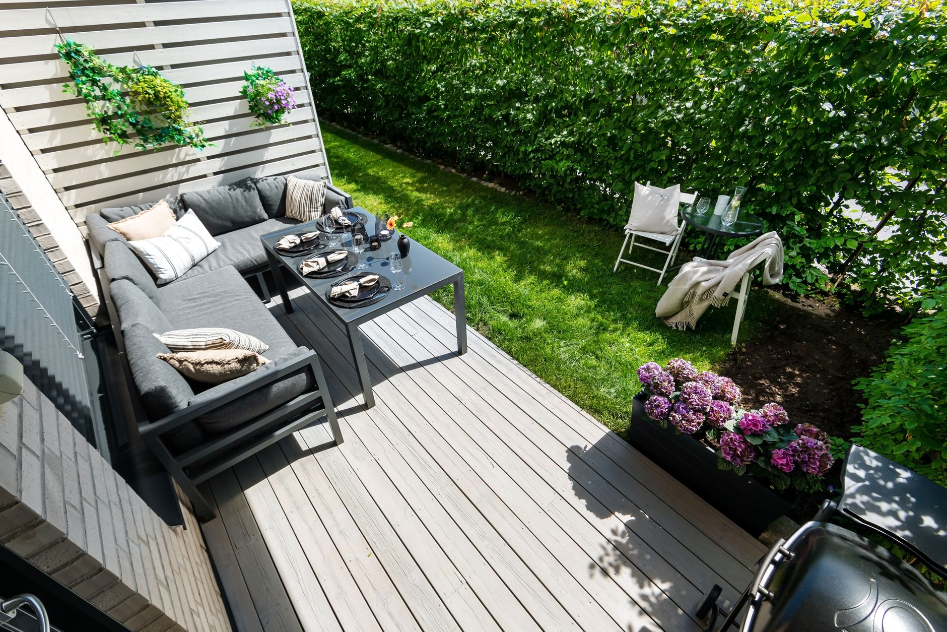 A backyard patio with outdoor seating, greenery, and a grill on a summer day
