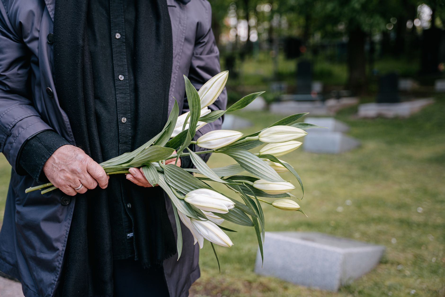A person holding white lilies in a quiet cemetery on a peaceful day