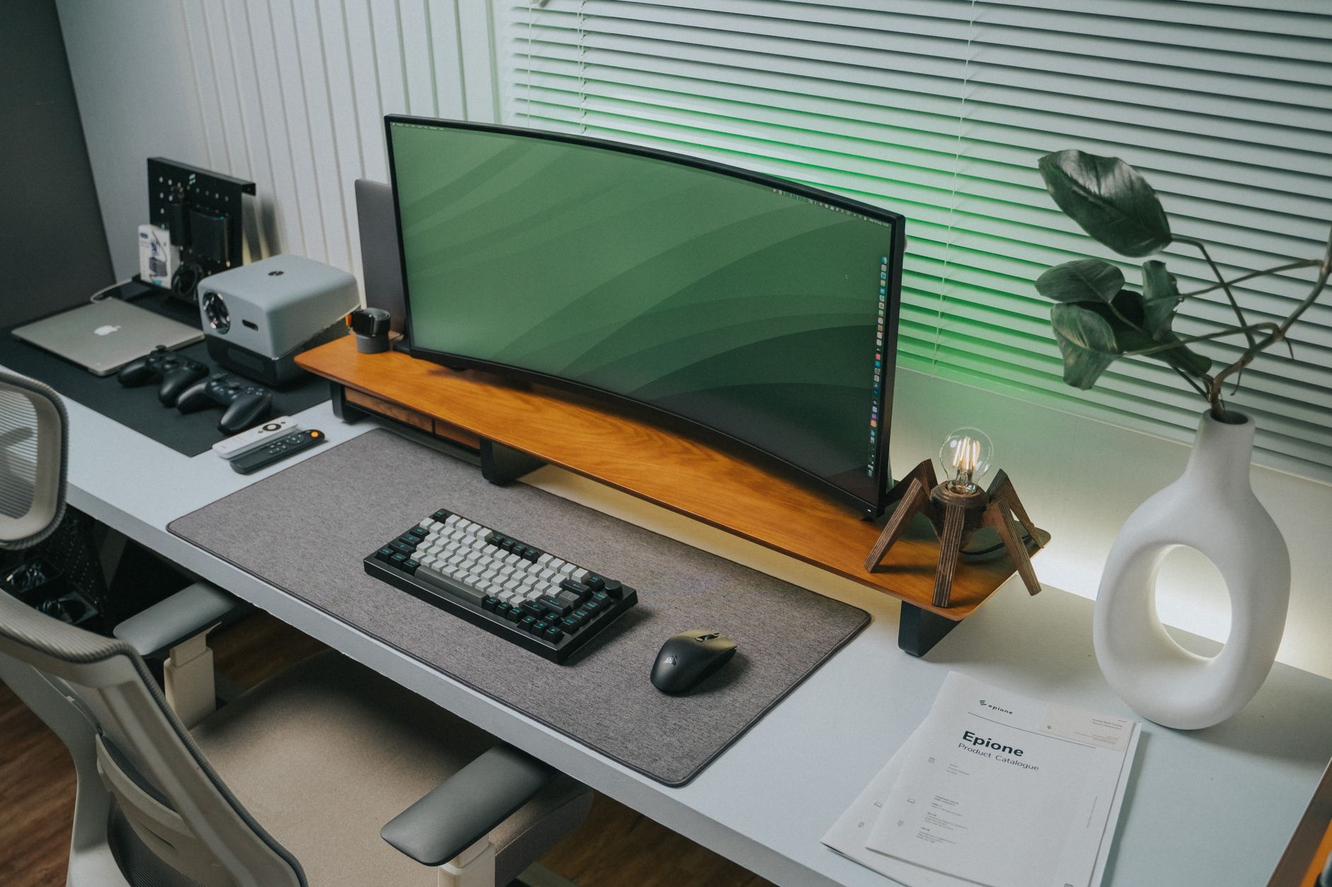 A tidy desk with a curved monitor beside a white vase of broad green leaves