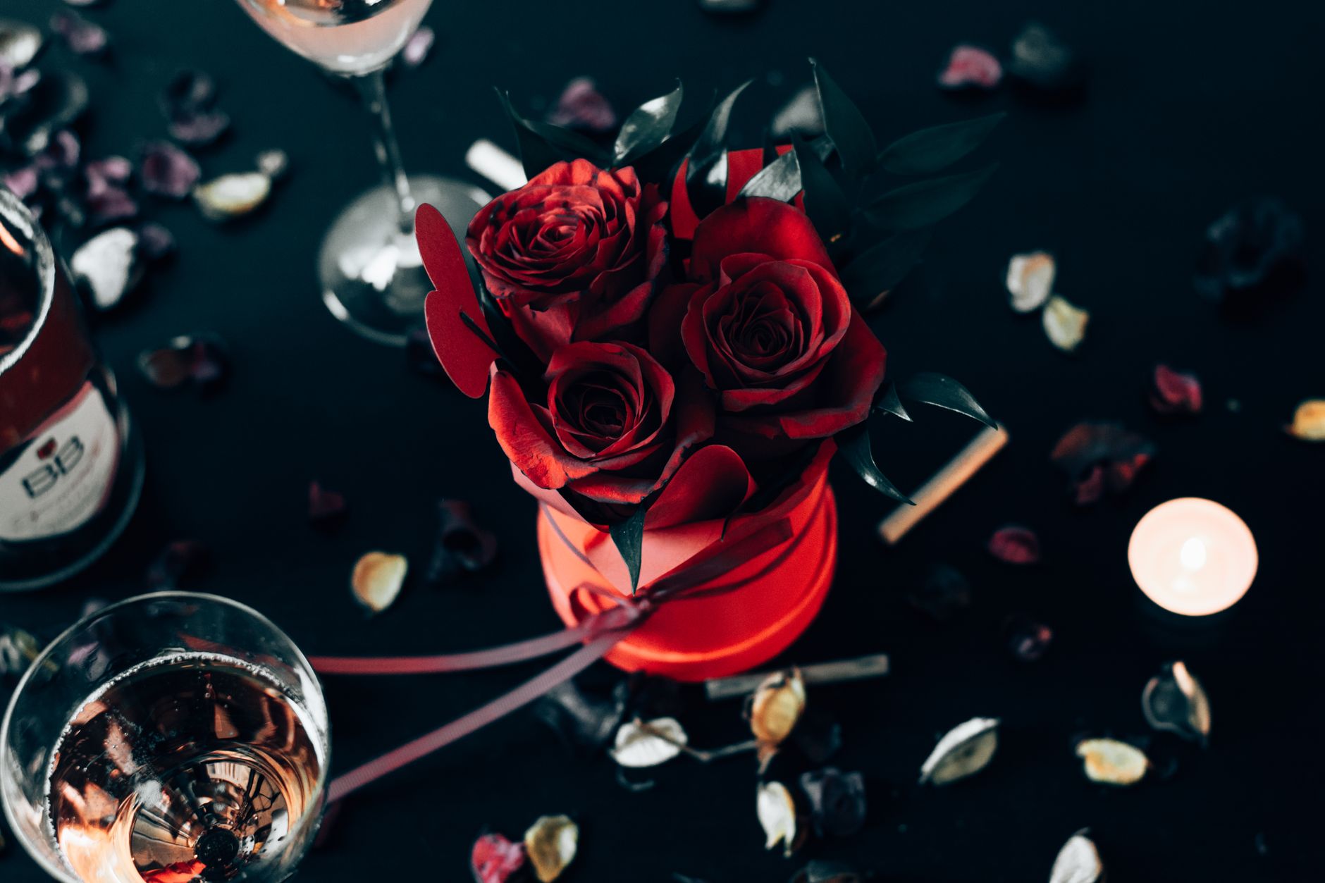 Red roses on a dark table with champagne glasses, petals, and candlelight