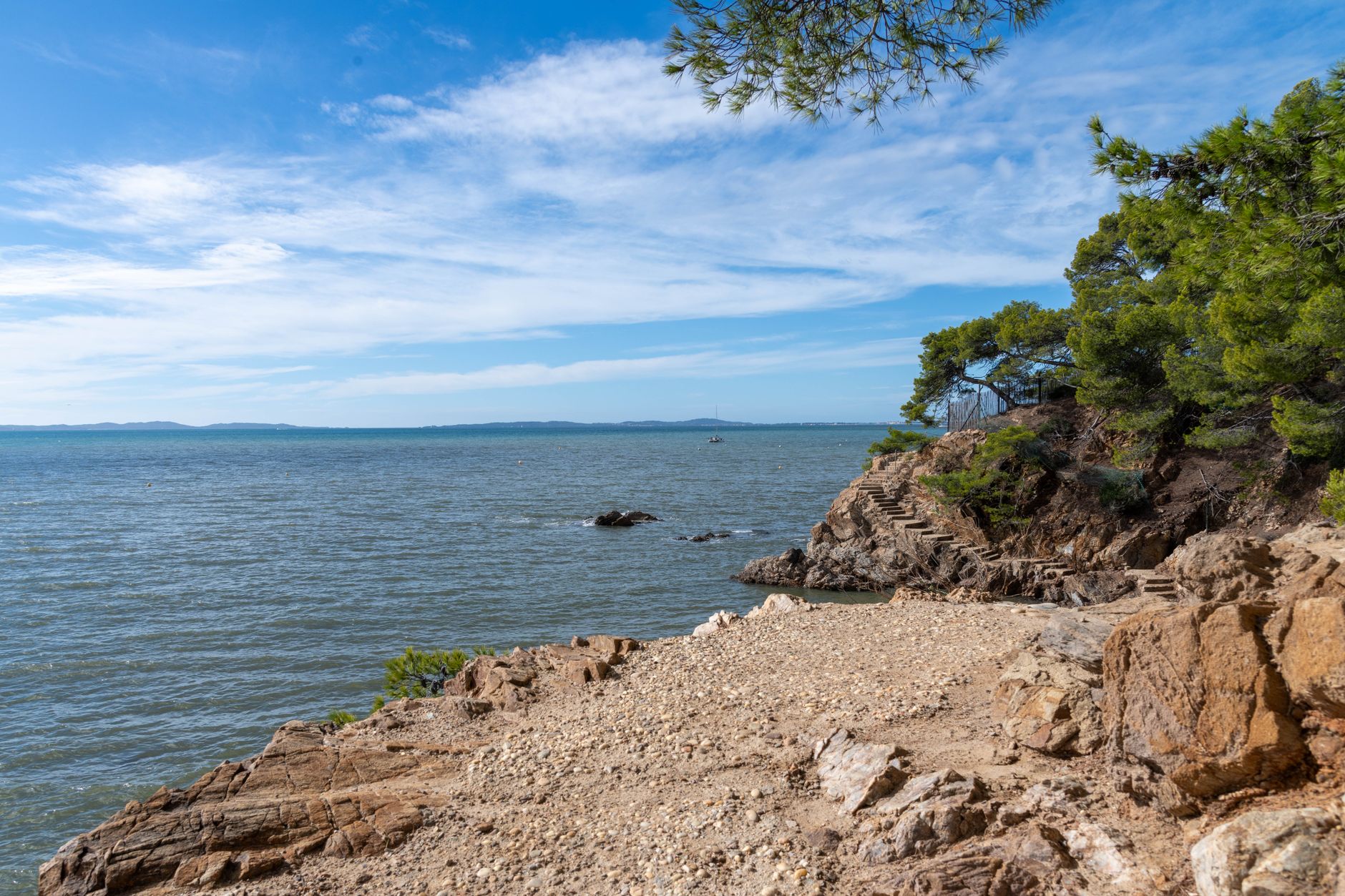 A rocky coastal shoreline curving beside calm blue water under a clear sky