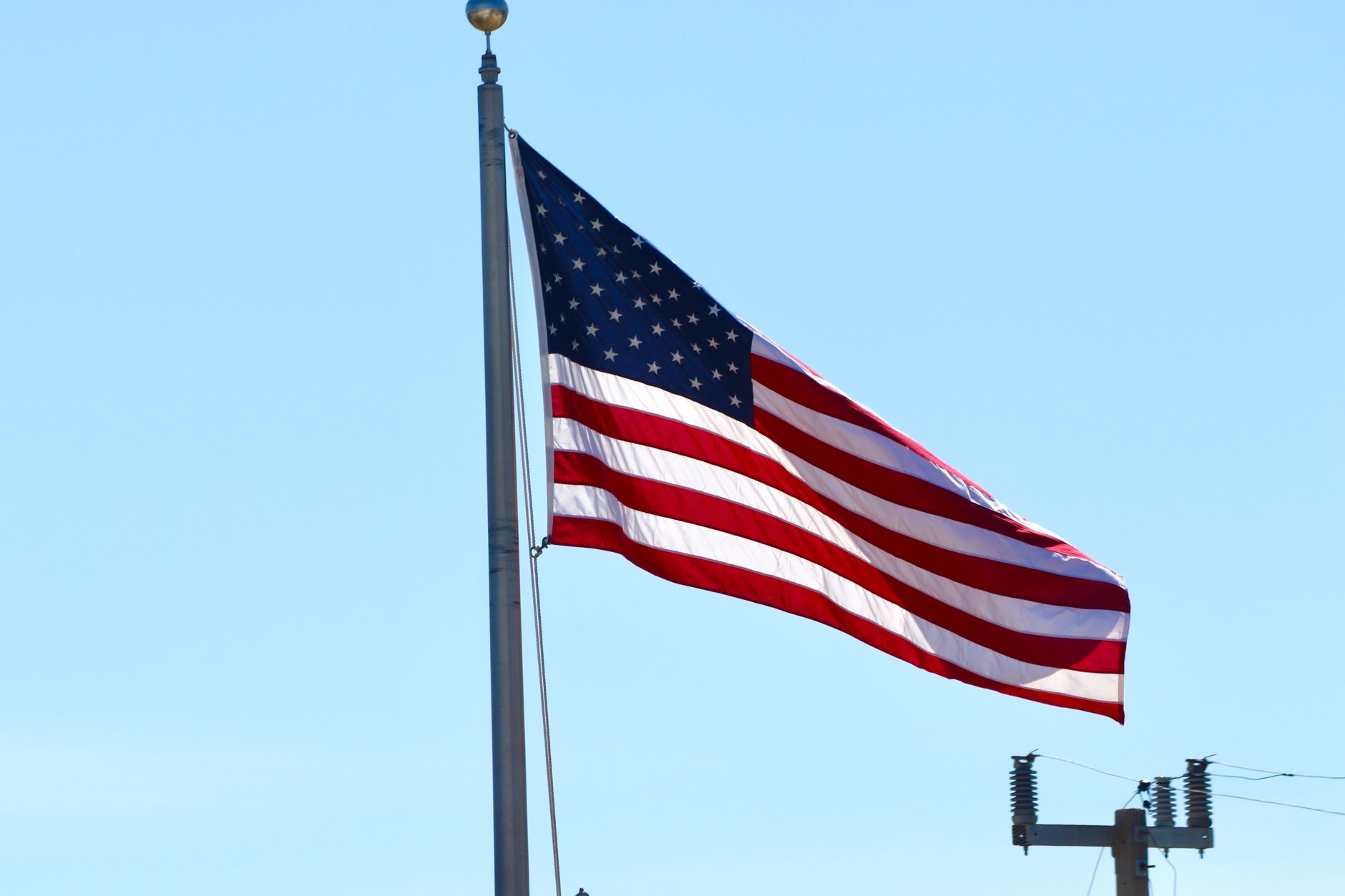An American flag flying from a tall pole against a clear blue sky