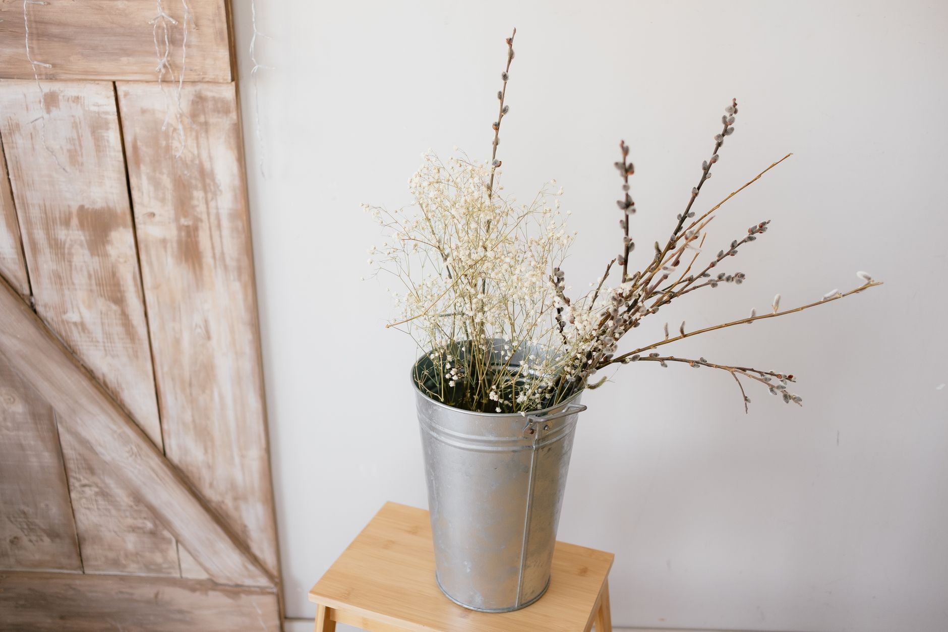 A metal bucket on a stool holding bare branches and delicate white filler flowers